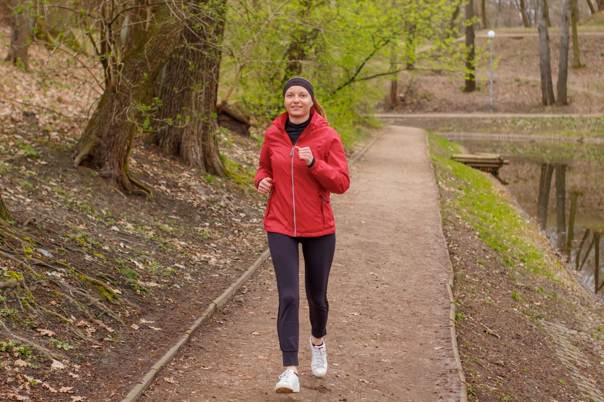 Donna con giacca rossa che corre sorridendo lungo un sentiero nel parco