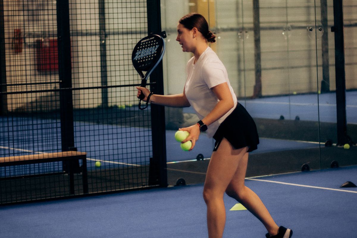 Giocatrice di padel con racchetta e palline su un campo coperto