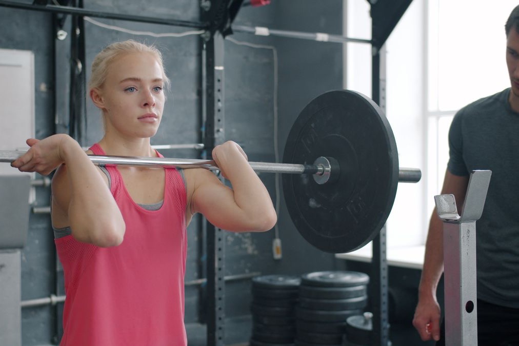 Ragazza che si allena con il bilanciere in palestra seguita da un istruttore